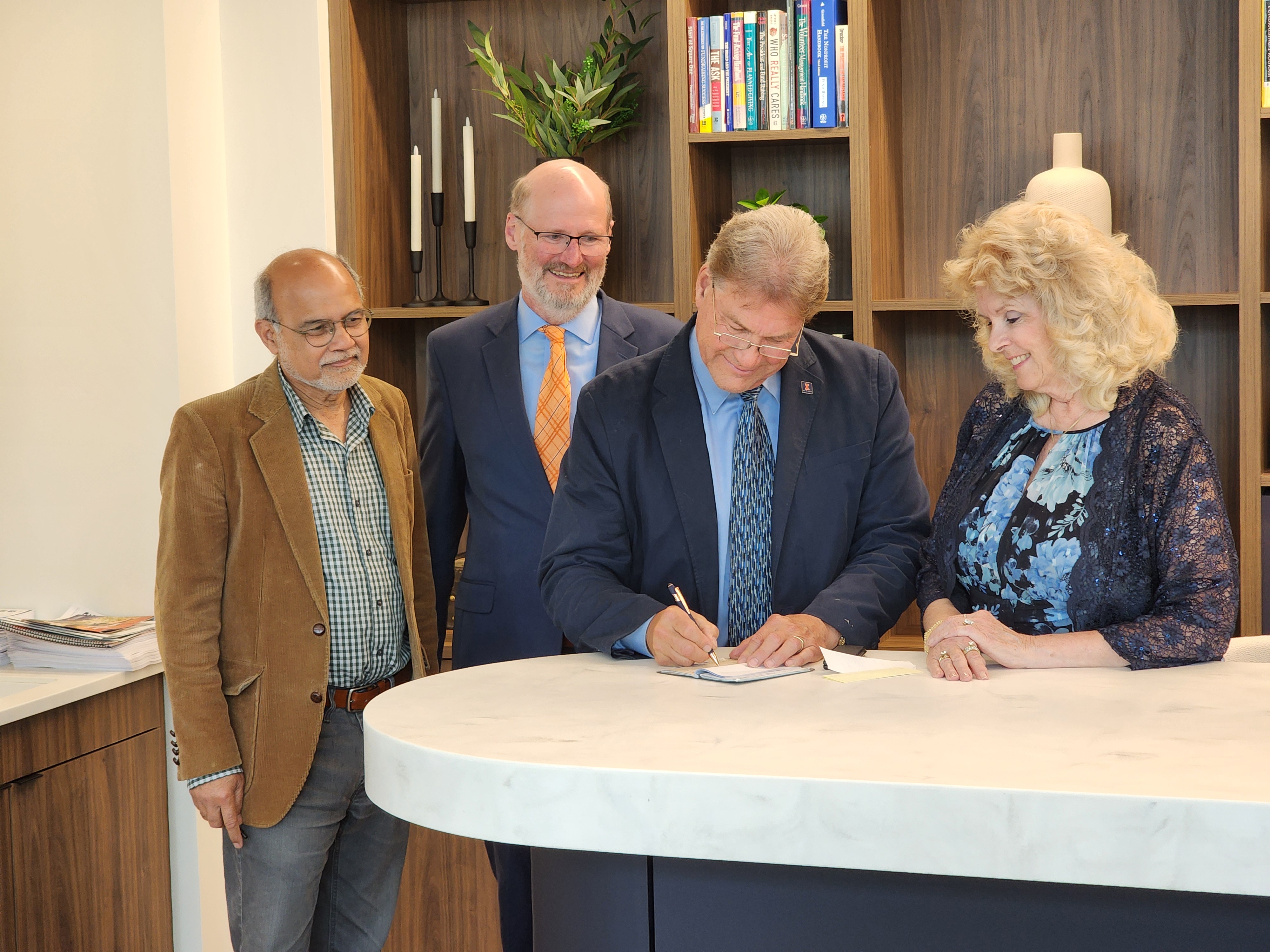 NPRE professor emeritus David Ruzic, center right, signs paperwork at the UIF Philanthropy Center, accompanied by department head Rizwan Uddin, left, Grainger College of Engineering associate dean Philippe Geubelle, and Marilyn Ruzic. (Photo Credit: Mike Lee/UIF)